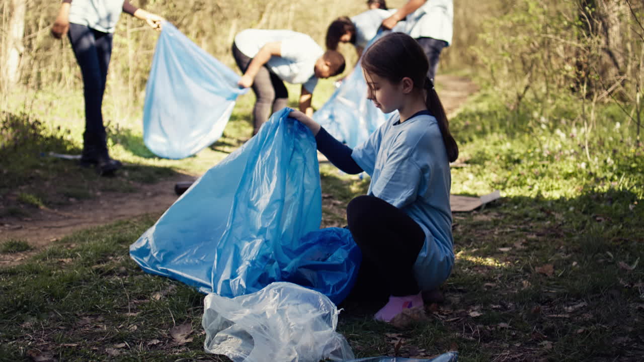 Tired little girl collecting trash and plastic bottles from the forest