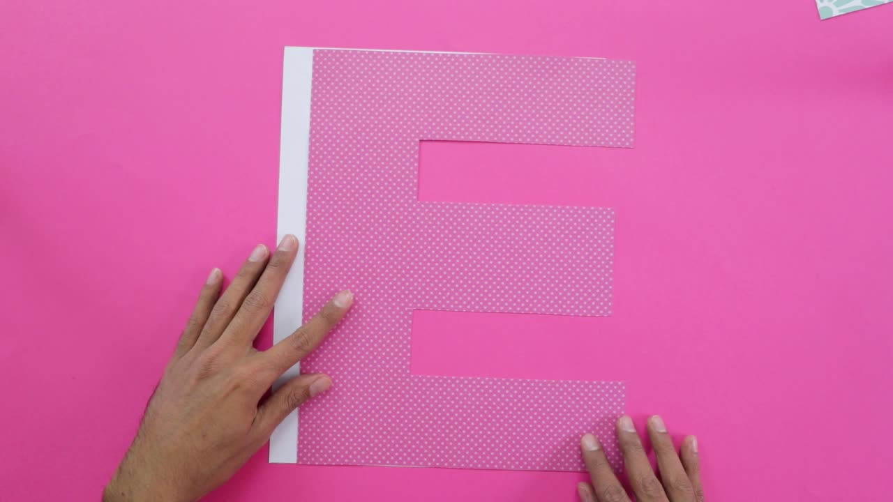 Aligning letter E cutouts from decorated paper on pink tablecloth.