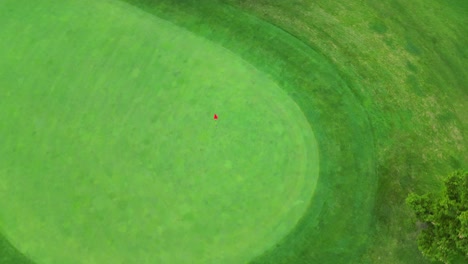 Un-Dron-Disparó-Sobre-Un-Putting-Green-Perfectamente-Cuidado,-Un-Asta-De-Bandera-Con-Una-Bandera-Roja