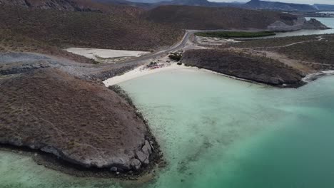 Toma-Aérea-De-Una-Hermosa-Zona-Costera-Con-Mar-Turquesa-Tranquilo,-Carretera-Costera-Y-Paisaje-Seco-En-Playa-El-Tecolote-Cerca-De-La-Paz-Baja-California-Sur-México