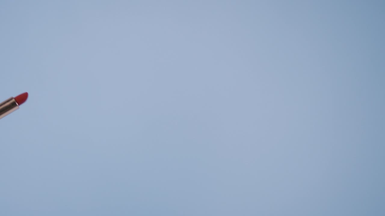 Playful redhead model with fair skin interacts with lipstick and draws shapes in the air while smiling.