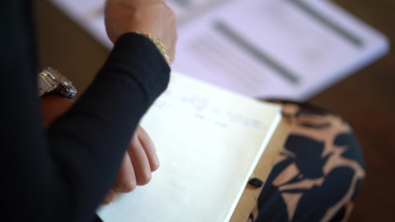 anciana escribiendo en un cuaderno con bolígrafo multicolor y luego tirando hacia atrás de su mano