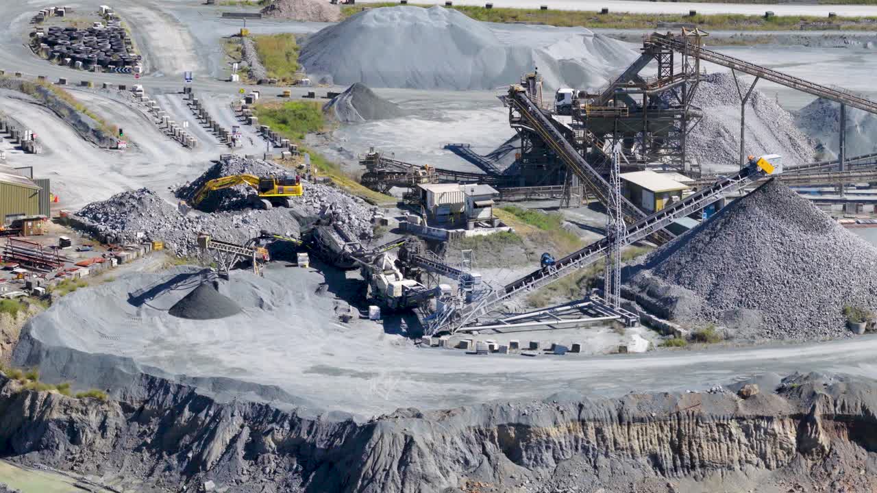 Drone captures active quarry with excavators and trucks moving stone under bright daylight, showcasing industrial mining activity