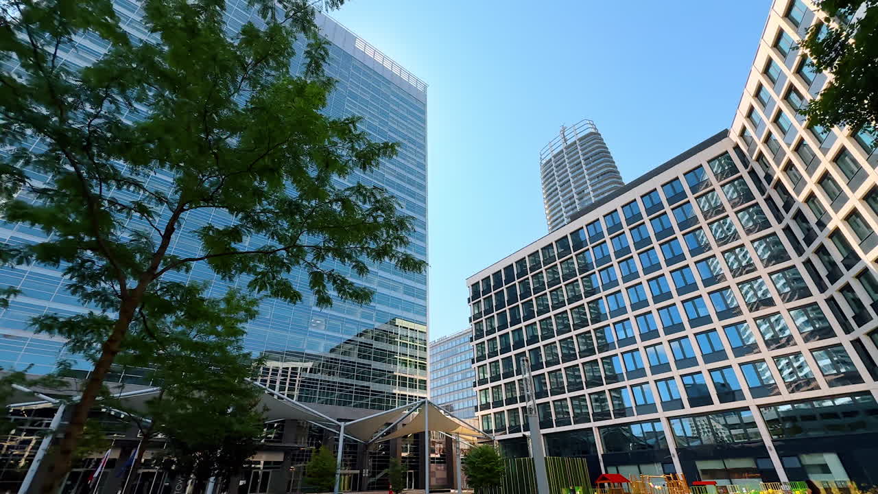 Urban modern architecture. Tall buildings reflect sunlight as people walk through the vibrant plaza beneath a clear blue sky