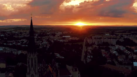 Vista-Aérea-Giratoria-De-La-Ciudad-De-Olomouc-De-La-República-Checa,-Que-Muestra-La-Torre-De-La-Iglesia-Contra-El-Sol-Rojo-En-La-Ciudad-Durante-La-Puesta-De-Sol