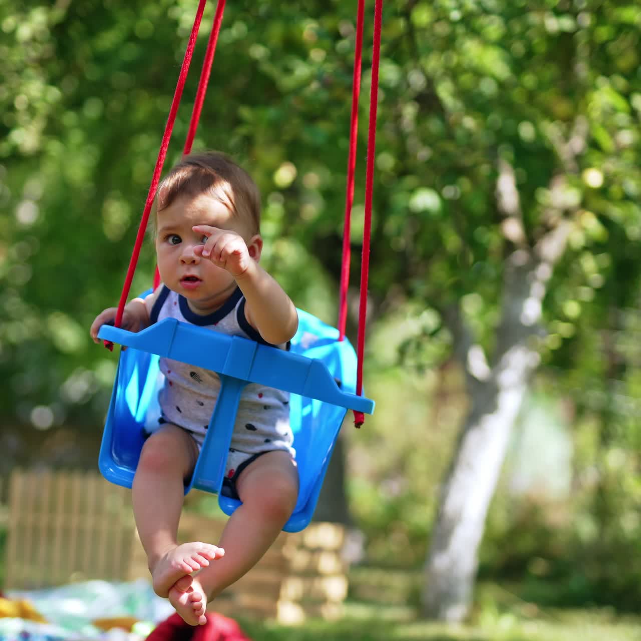 Adorable little kid sitting in a swing. Lovely calm boy waving his hand while swinging. Nature backdrop