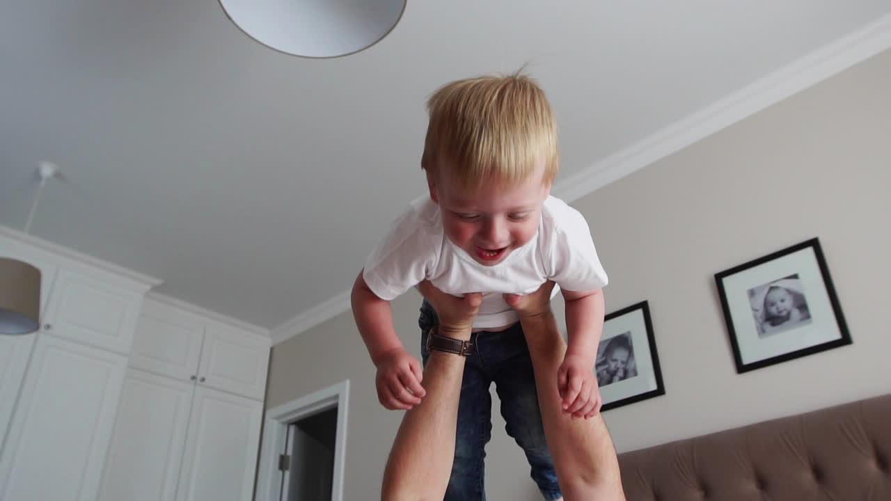 Dad keeps a dignity above himself lying on the bed. A boy in a white T-shirt laughs and smiles from playing with his father