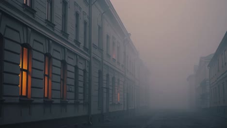 dense fog envelops a deserted city street at dawn, with the warm glow of illuminated windows emanating from the buildings, creating a mysterious and atmospheric urban scene