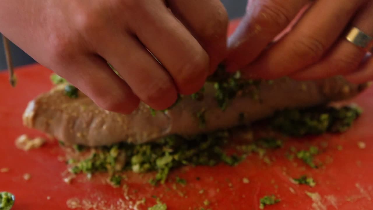 Small loaf of meat rolled in herbs, greens, preparing for baking. Close up.