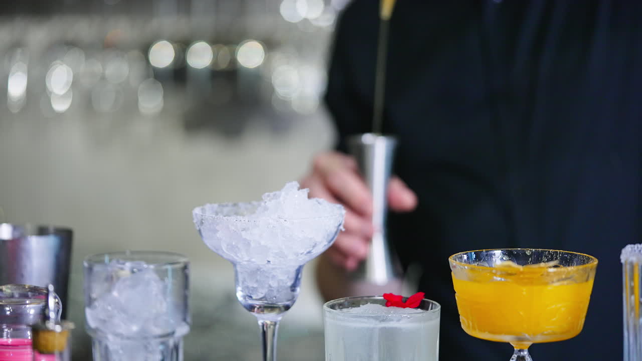 Diverse glasses with ice and liquid stuff. Unrecognized bartender filling the beaker with yellow liquid and pours it into glass. Blurred backdrop.