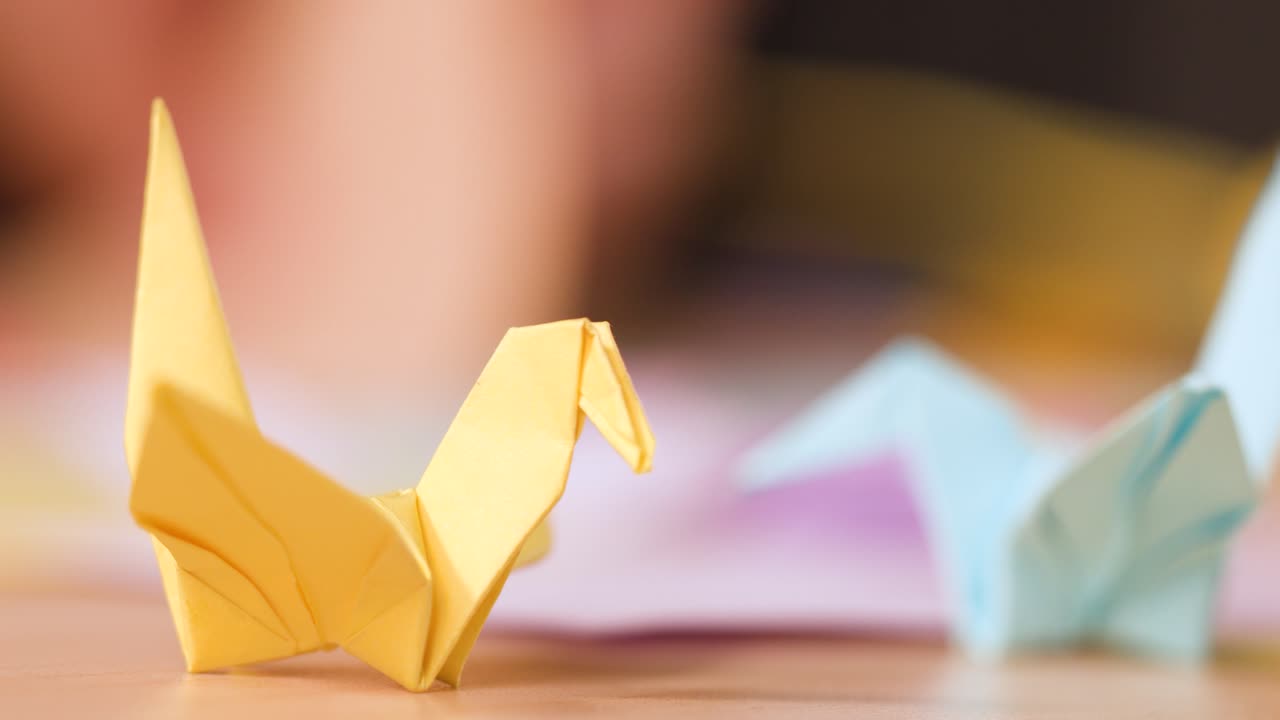 Nærbillede af hænder, der omhyggeligt folder en gul papirkran på et arbejdsbord af træ