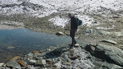 Male-hiker-crosses-mountain-stream-by-using-stepstones,-reflection