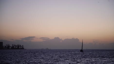 single boat sailing on river tejo with industrial buildings on the left during sunset