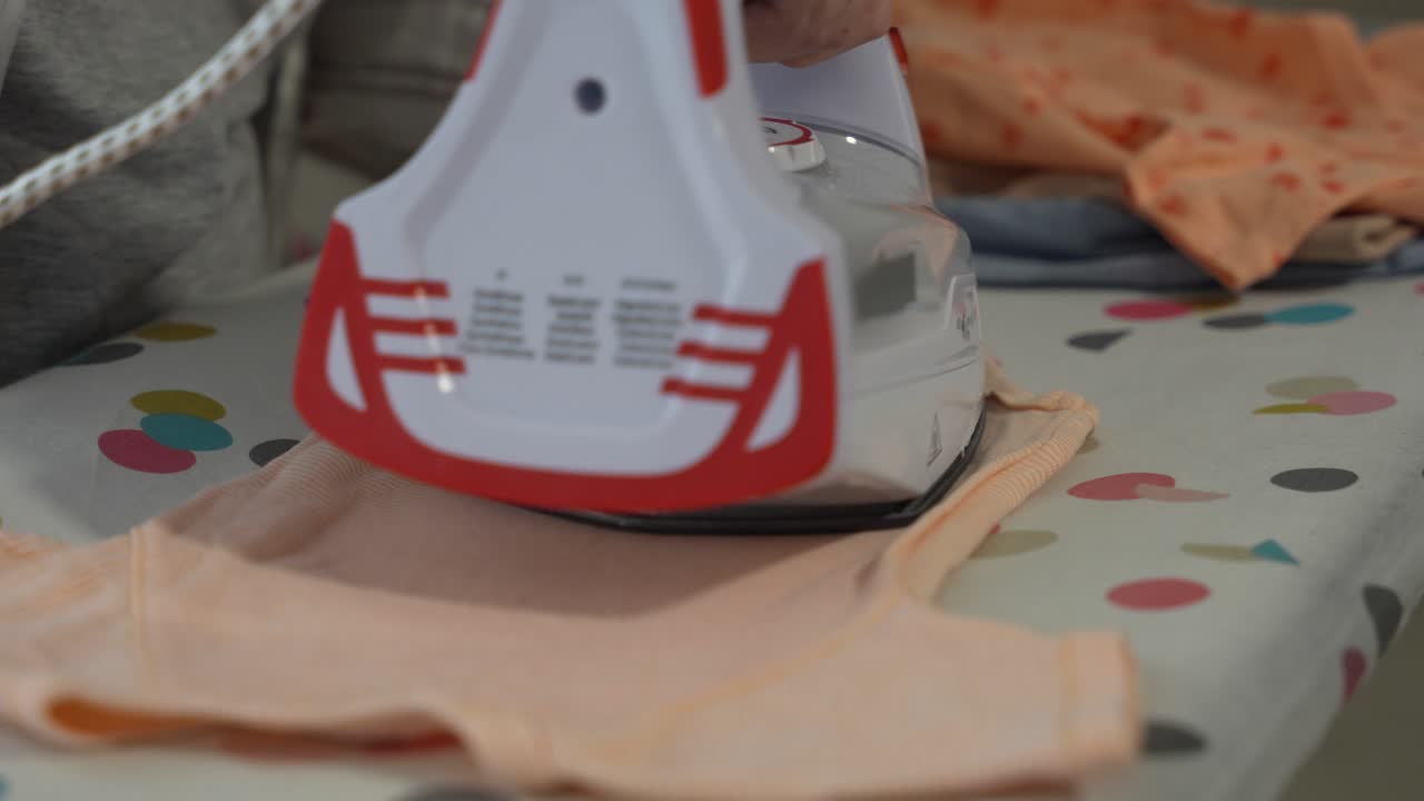 Close up shot of baby bodysuit being placed on board for ironing at home