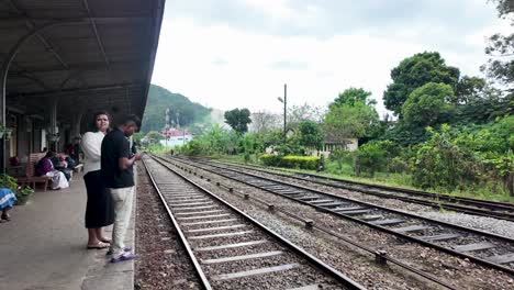 a couple waits patiently at the picturesque haputale railway station in sri lanka, taking in the serene surroundings and lush greenery while checking their mobile phones.
