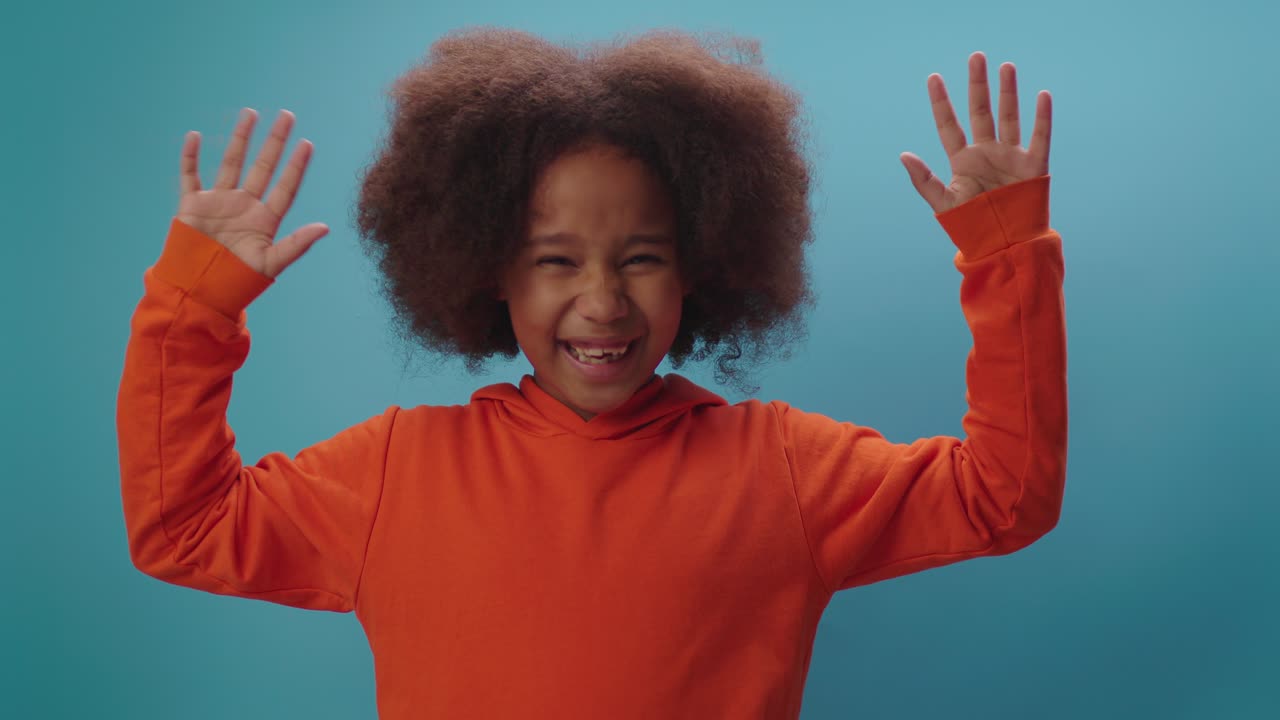 una alegre chica afroamericana levantando las manos como un signo de triunfo de pie sobre un fondo azul. feliz de ganar.