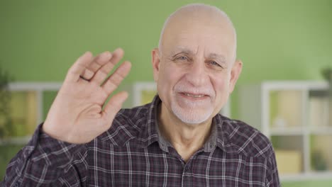 Sympathetic-old-man-smiling-looking-at-camera-and-waving,-saying-hello.