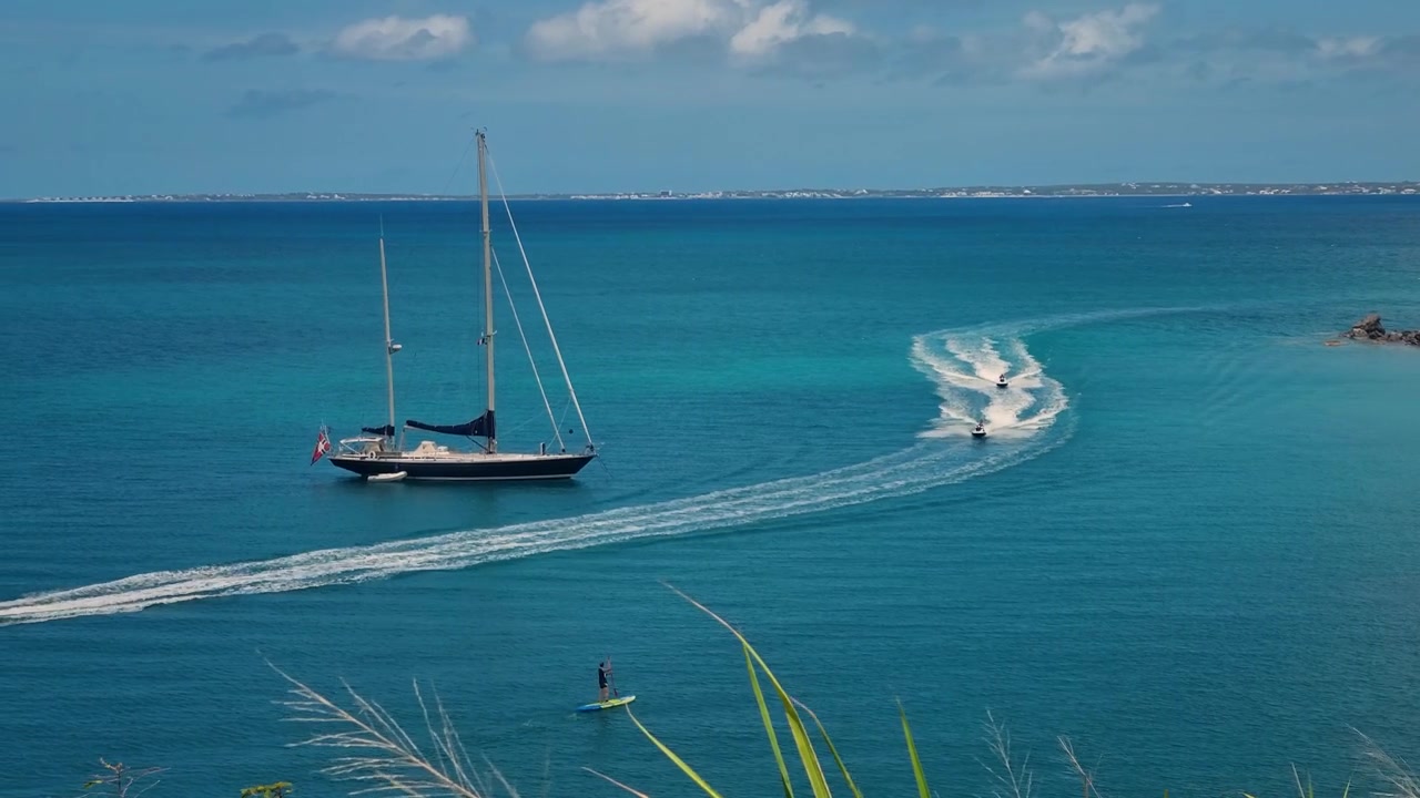 Moto d'acqua sfrecciano attraverso le acque turchesi dei Caraibi al largo di St. Martin, Sint Maarten, con uno yacht a vela e un praticante di stand-up paddle in vista. Paradiso tropicale per le vacanze con Anguilla all'orizzonte.