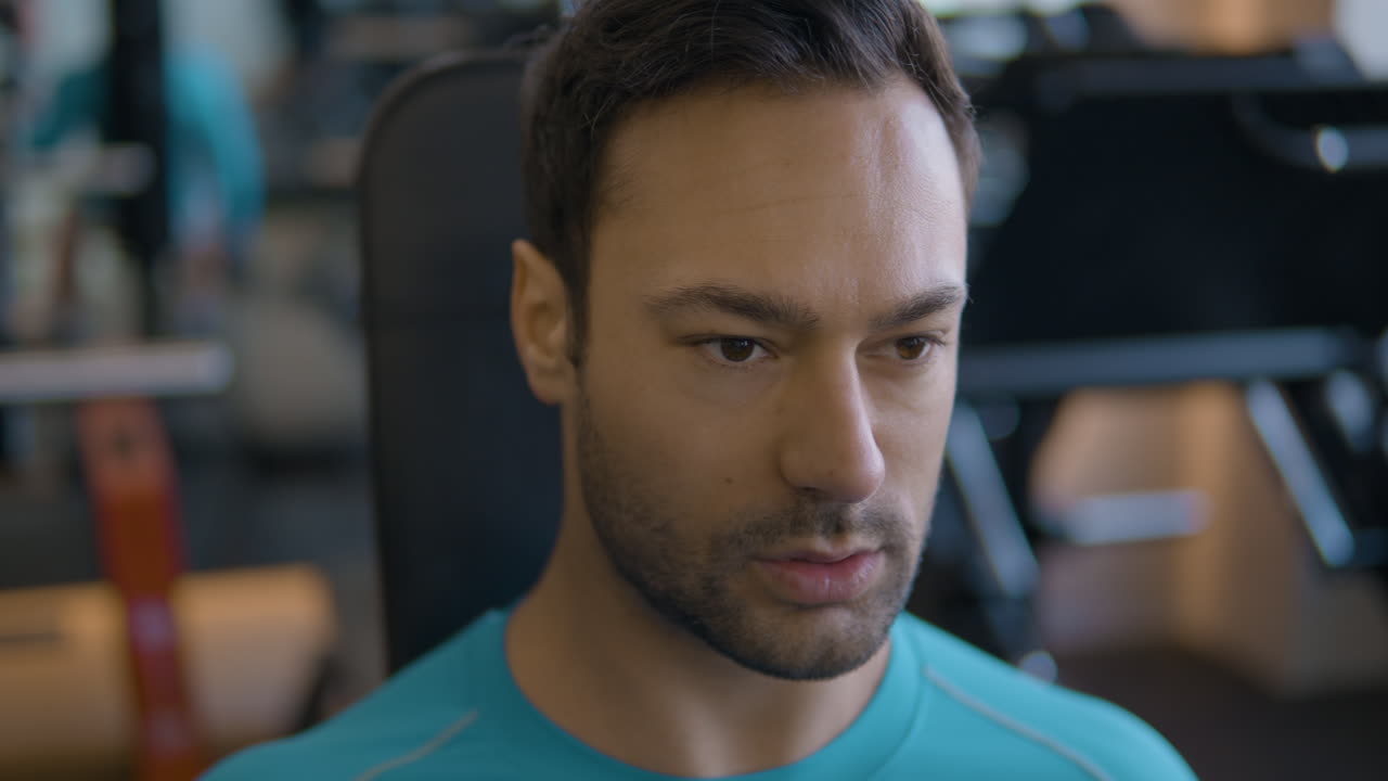 Ritratto di uomo mentre esegue curl bicipiti con manubri da seduto in palestra.