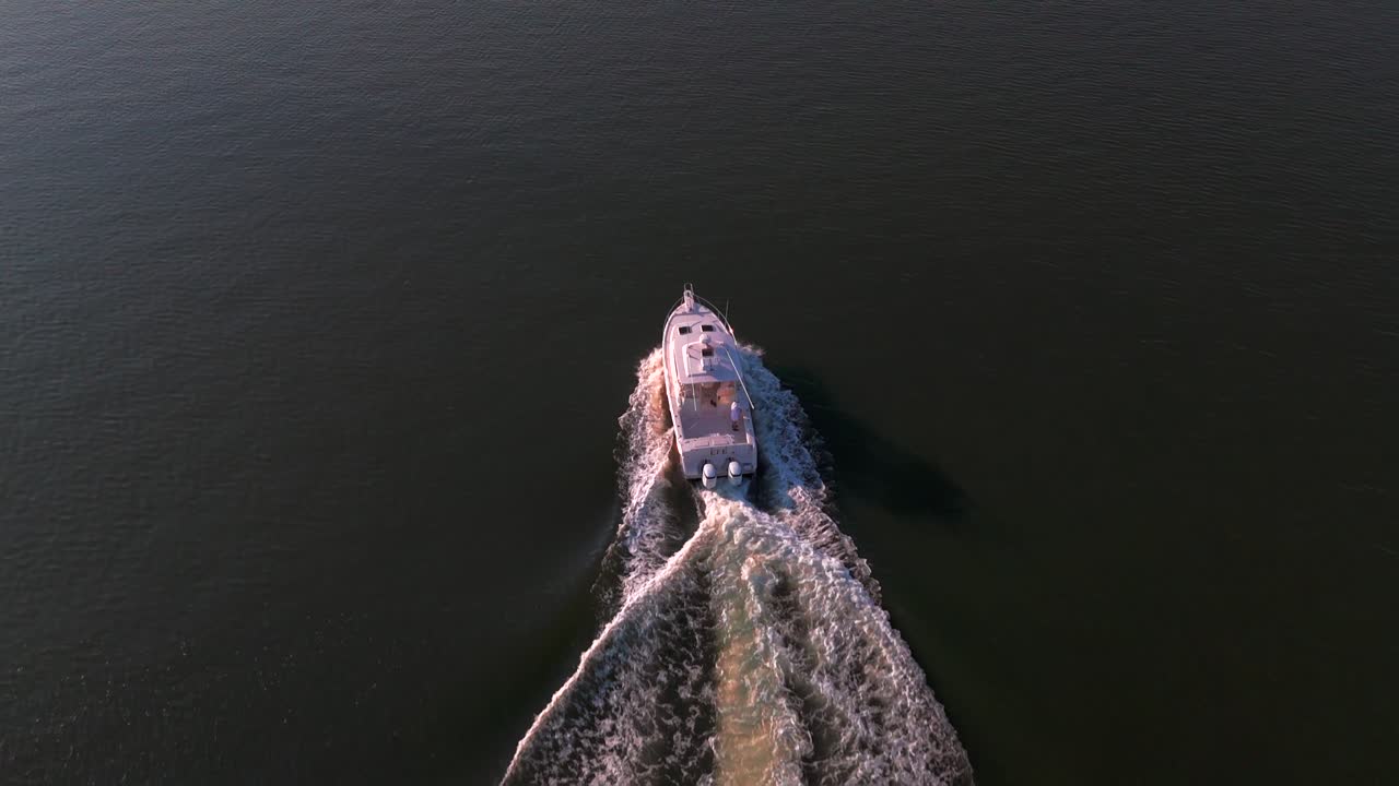 An aerial view, following a white fishing boat in the bay off the southern shores of Long Island, NY on a sunny day. The camera dolly in, truck left and fly over and past the vessel