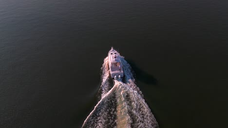 an aerial view, following a white fishing boat in the bay off the southern shores of long island, ny on a sunny day. the camera dolly in, truck left and fly over and past the vessel