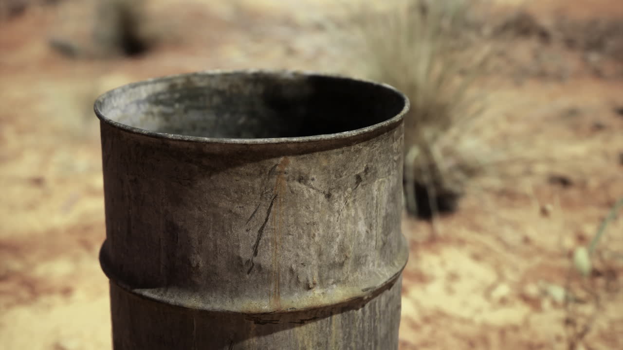 Rusty barrel stands alone in a barren landscape under a bright sky