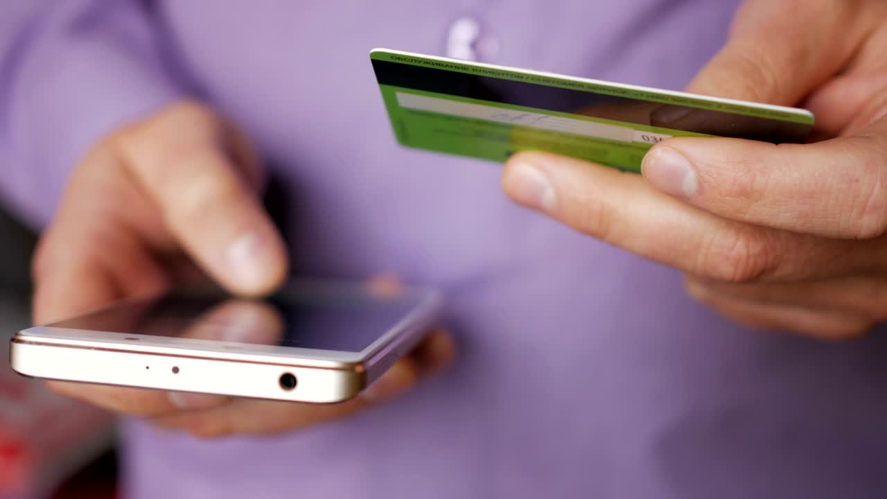 hombre de negocios con una camisa púrpura haciendo pago en línea con tarjeta de crédito y teléfono inteligente, compras en línea, tecnología de estilo de vida. hombre introduce el número de tarjeta bancaria en el teléfono inteligente. primer plano. primer plano