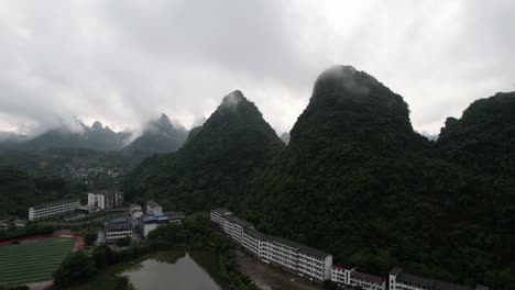 Vuelo-Aéreo-Hacia-Atrás-De-La-Montañosa-Ciudad-De-Yangshuo-Cubierta-Por-Nubes,-China