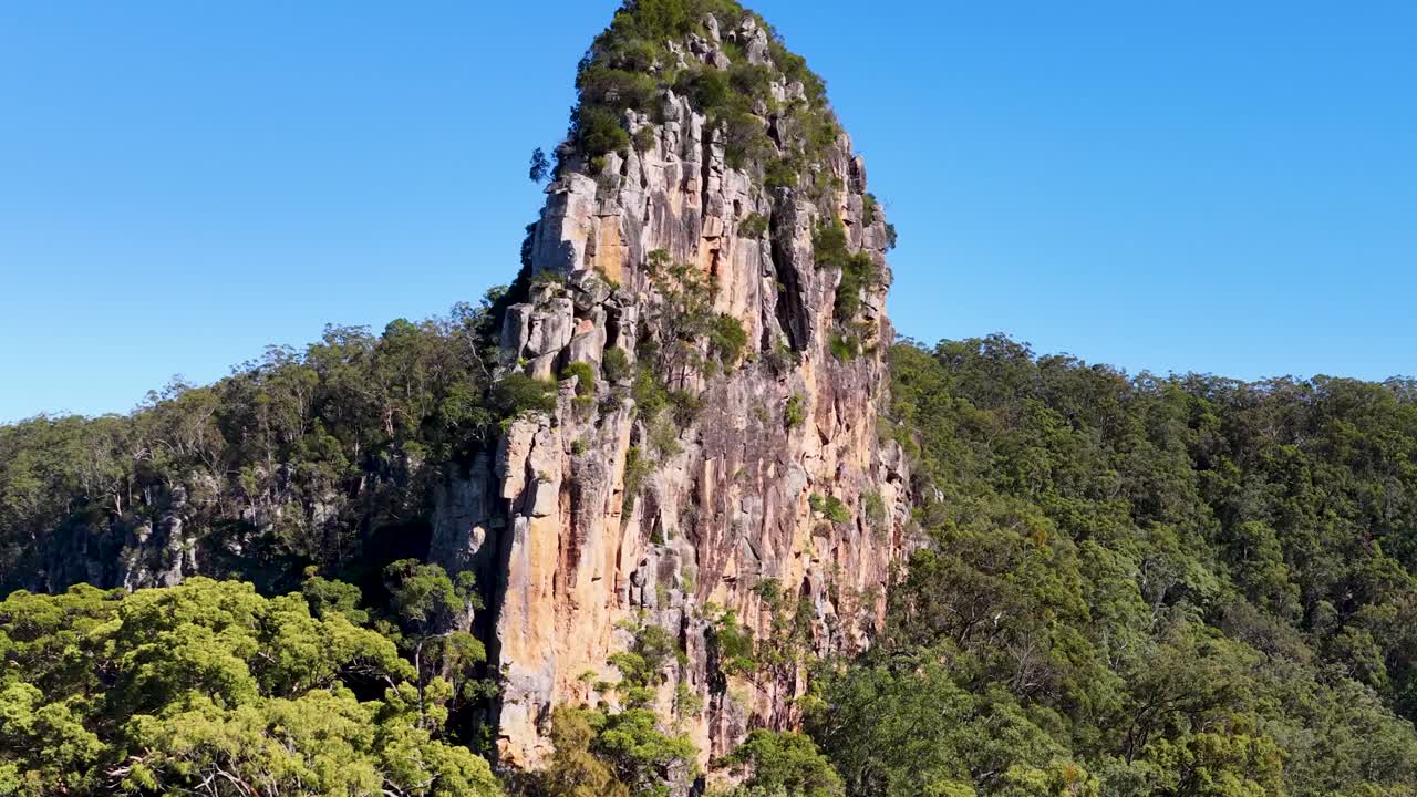 Aerial footage capturing the majestic Nimbin Rocks against a clear blue sky, highlighting their rugged texture and surrounding greenery