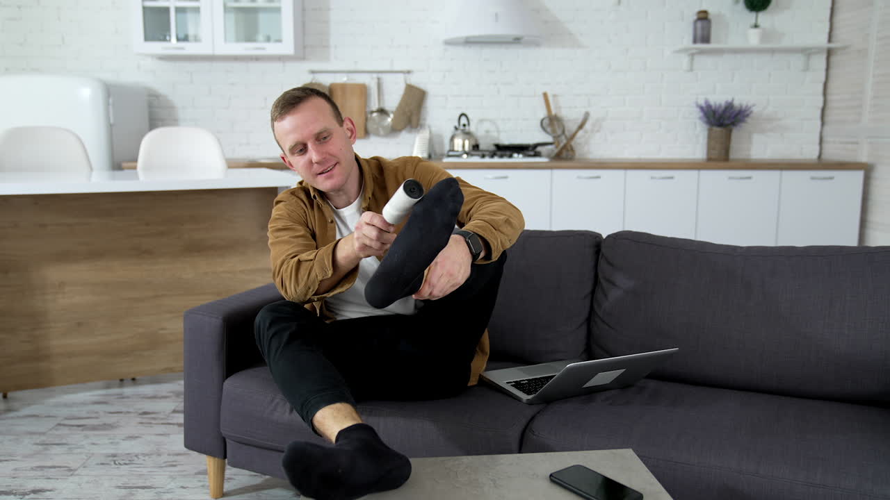 Man on sofa at home. Young man resting at home, brushing his socks