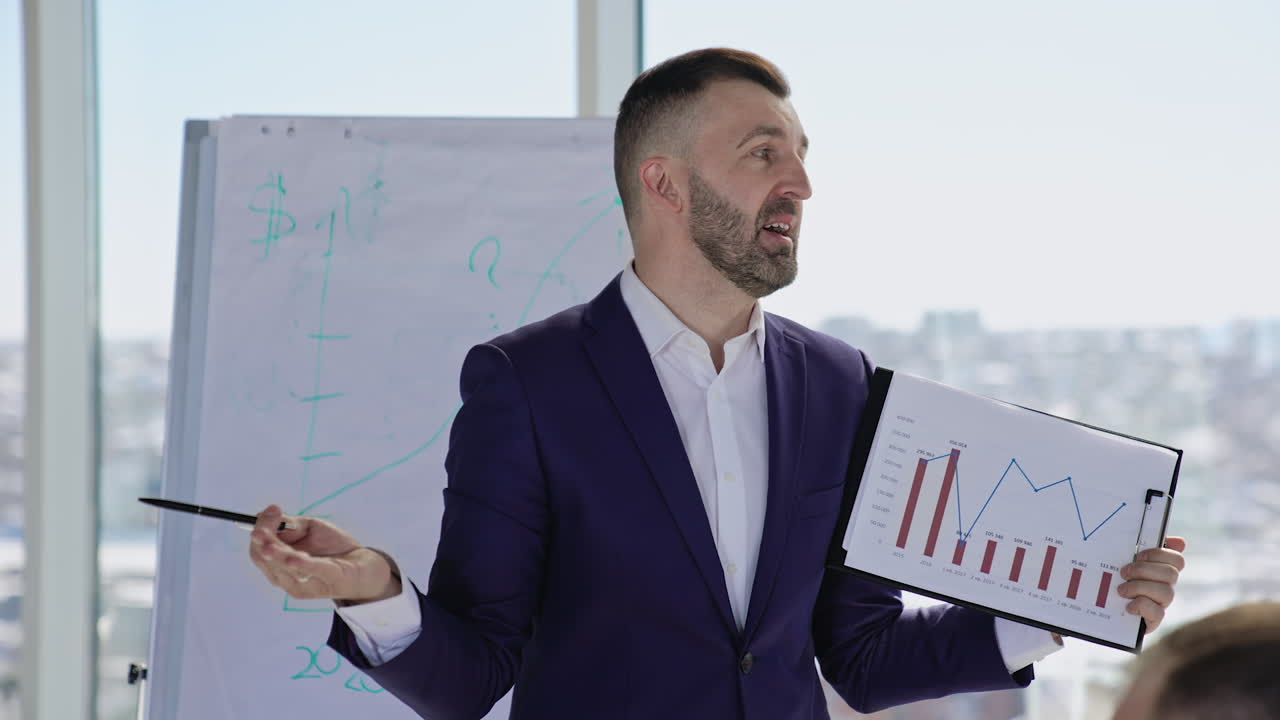 Confident positive bearded man talks to the public holding chart in his hand. Businessman showing the results of company work at the meeting.
