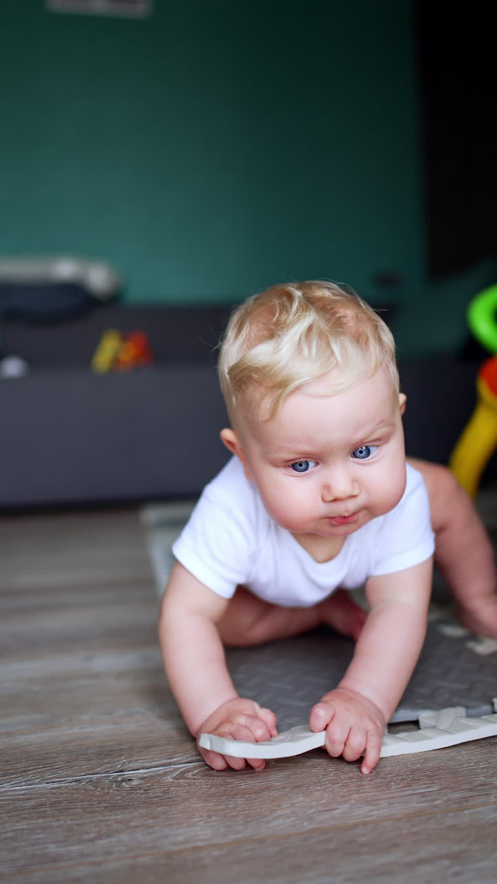 Adorable baby boy half-lying on the floor. Lovely kid sits up chewing the item. Vertical video.