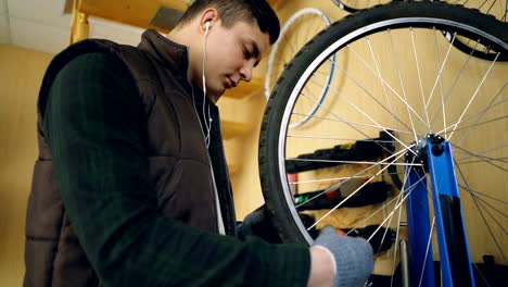concentrated mechanic is fixing spokes on bicycle wheel with special tools while servicing bike and listening to music through earphones. maintenance and profession concept.