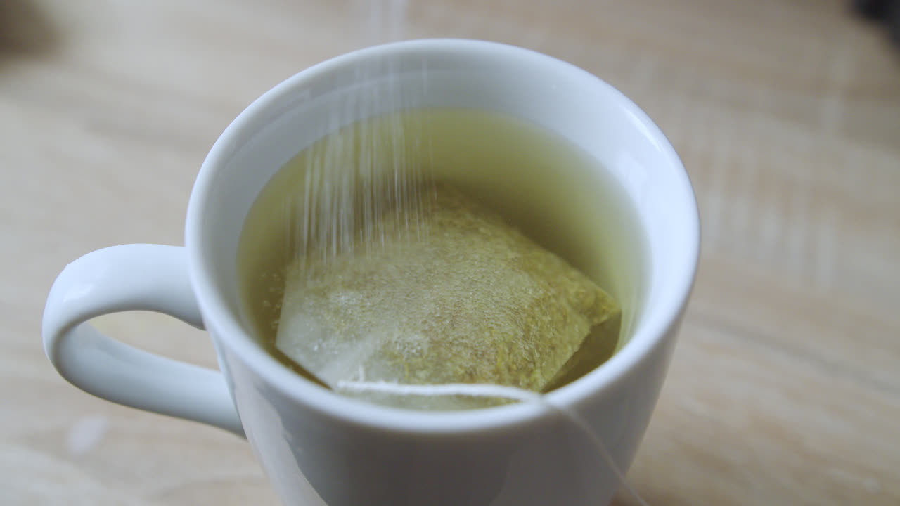 봉투 에서  설탕 을 는 동안 뜨거운 물 과 카모밀 을 가진  컵 의 아름다운 가까운 느린 동작