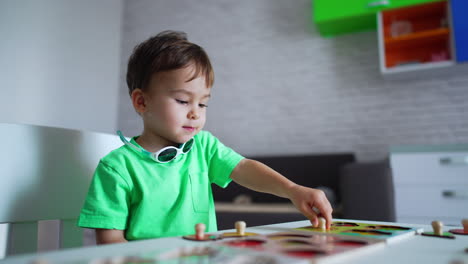 serious caucasian toddler playing at the desk. cute kid is busy with solving puzzles. blurred backdrop.