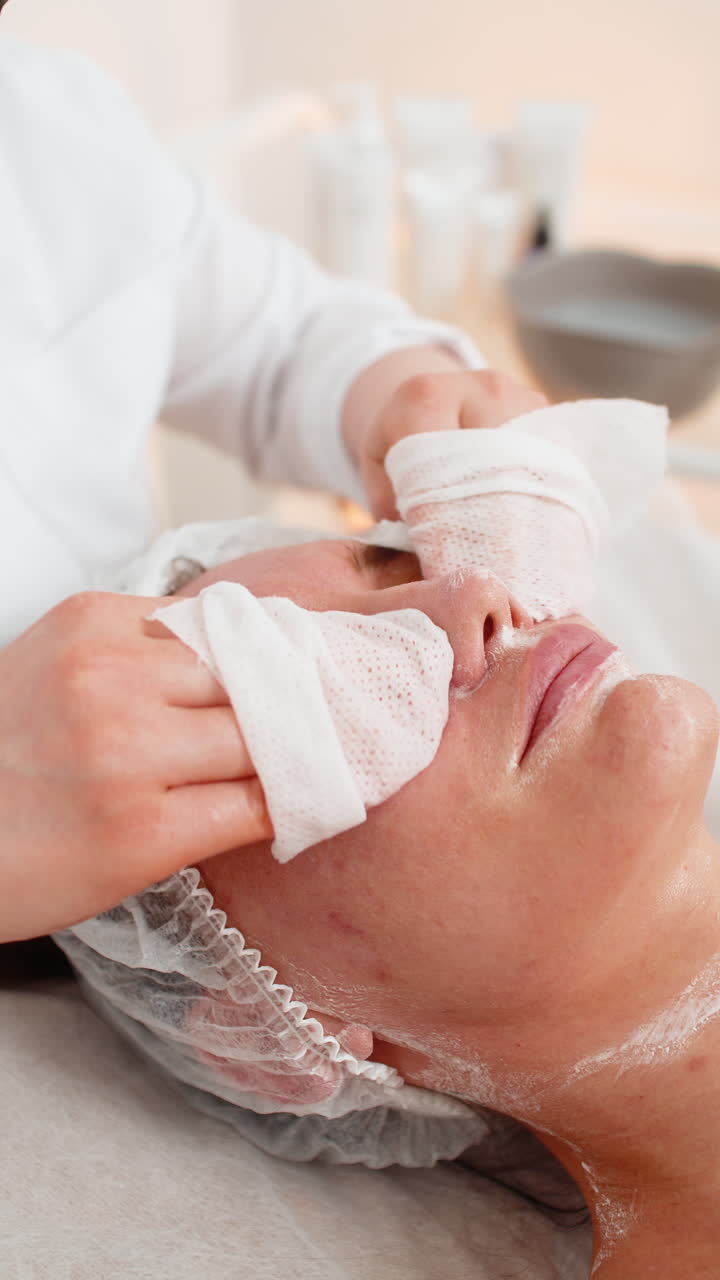Una dottoressa cosmetologa pulisce viso e collo di una donna durante una procedura di pulizia con dischetti di cotone in una clinica estetica