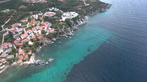 Vista-Aérea-De-La-Playa-Turquesa-Con-Rocas-Bajo-Un-Pueblo-Turístico-En-La-Zona-De-Agia-Paraskevi-Halkidiki,-Grecia,-Movimiento-Circular-Por-Drones