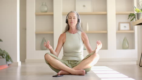 caucasian woman with gray hair meditating, wearing headphones