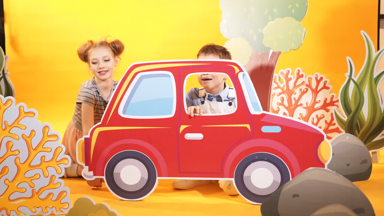 Funny children are playing with a big red car. Decorative background. Studio shooting of children