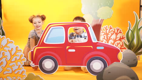 funny children are playing with a big red car. decorative background. studio shooting of children