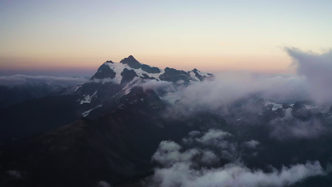 Panoramic aerial establishing view of Mt Shuksan northern cascade mountains at sunset with soft orange gradient glow in sky