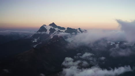 Panoramic-aerial-establishing-view-of-Mt-Shuksan-northern-cascade-mountains-at-sunset-with-soft-orange-gradient-glow-in-sky