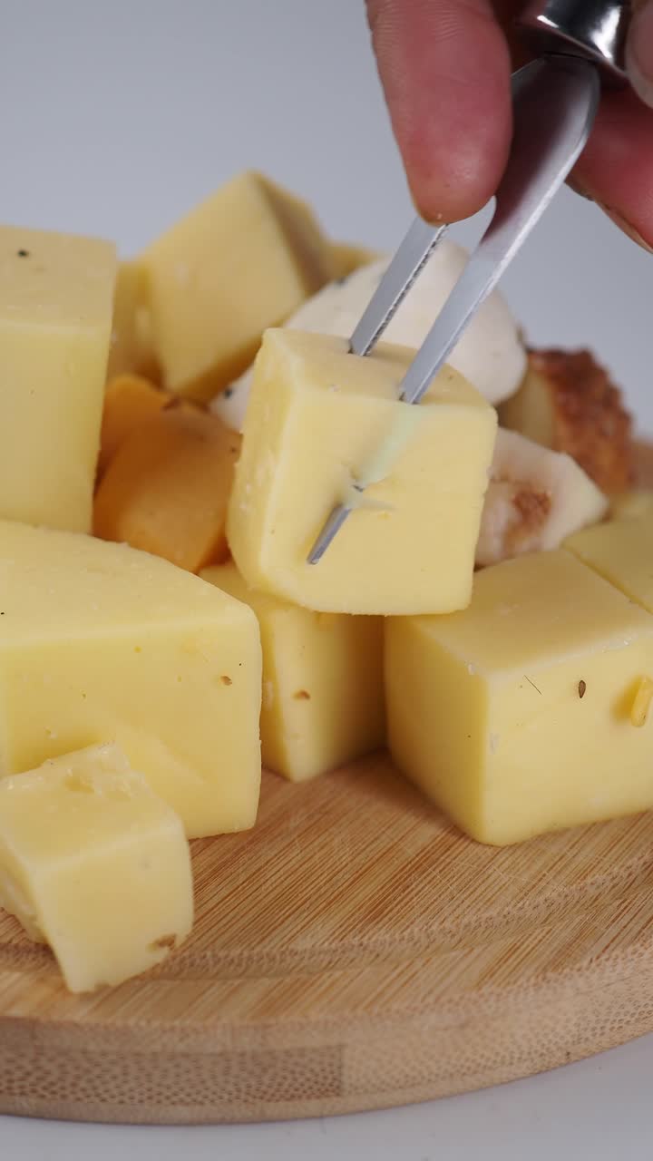 Mão pegando um cubo de queijo com uma pinça de uma tábua de madeira