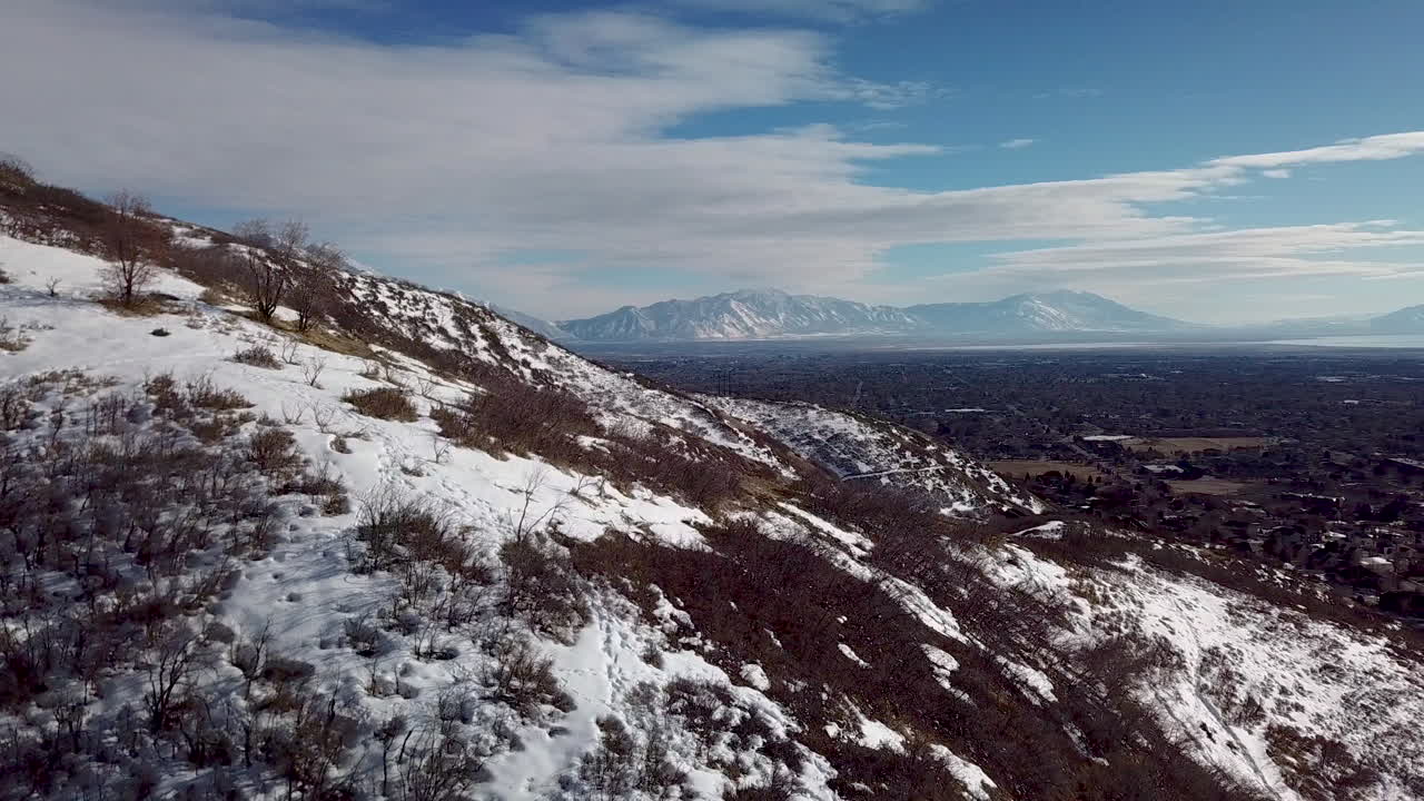 volando sobre las colinas para revelar una ciudad, un lago y montañas al otro lado del valle en invierno