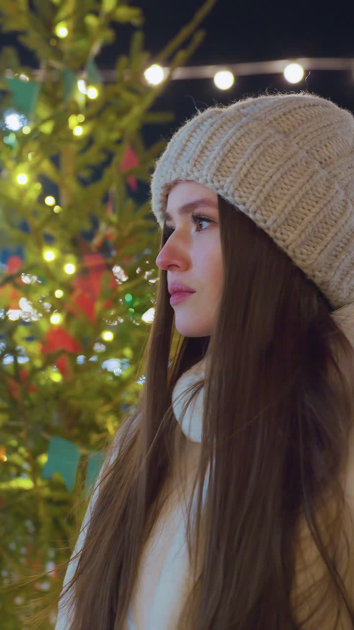 Young adult in warm winter outfit stands near festive Christmas tree, smiling as people skate in the background, holiday lights create a magical atmosphere filled with joy