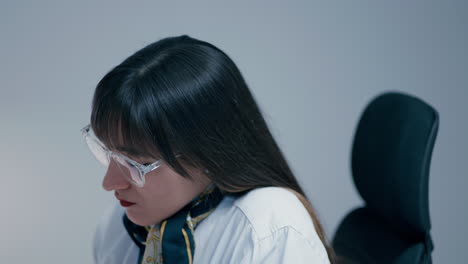 긴 어두운 머리카락을 가진 아름다운 젊은 여성이 안경을 입고 사무실에서 느린 동작으로 일에 집중하고 있습니다.