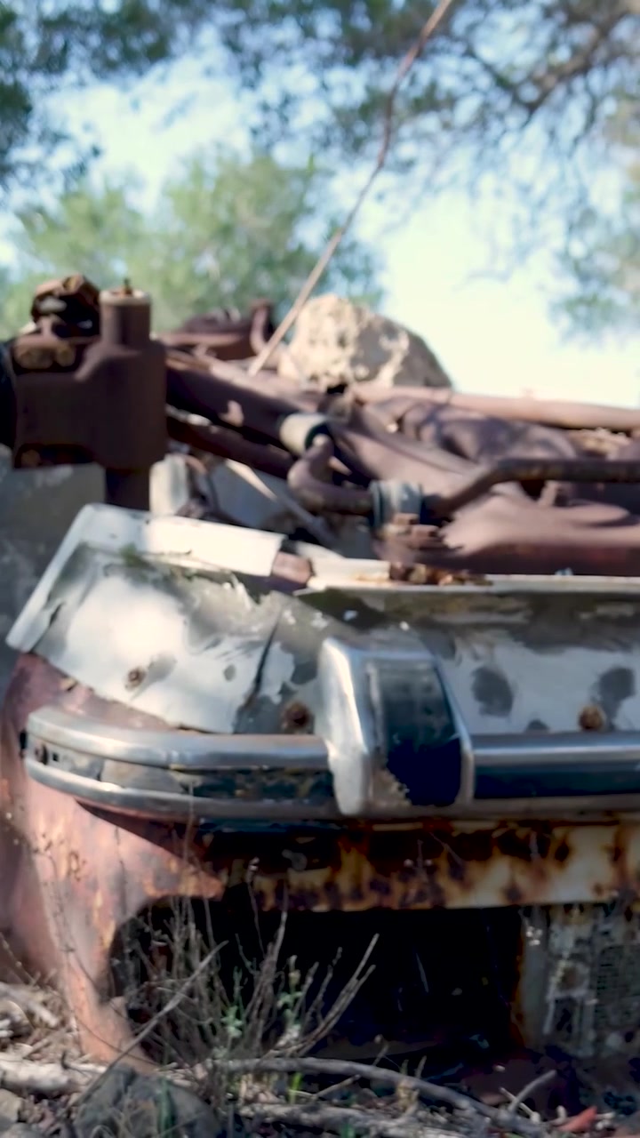 View of rusty abandoned vehicle frame with corroded metal and peeling paint resting on dry terrain with sparse vegetation on slopes of Mount Ainos in Kefalonia Greece