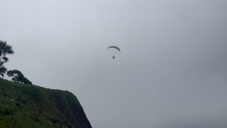 powered paraglider flies overhead towards clifftop