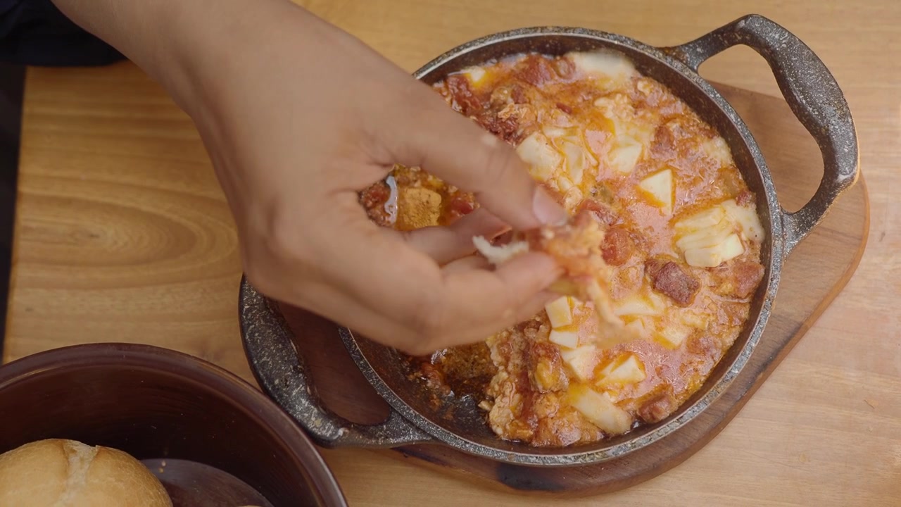 Persona che intinge il pane in una padella calda di Menemen.