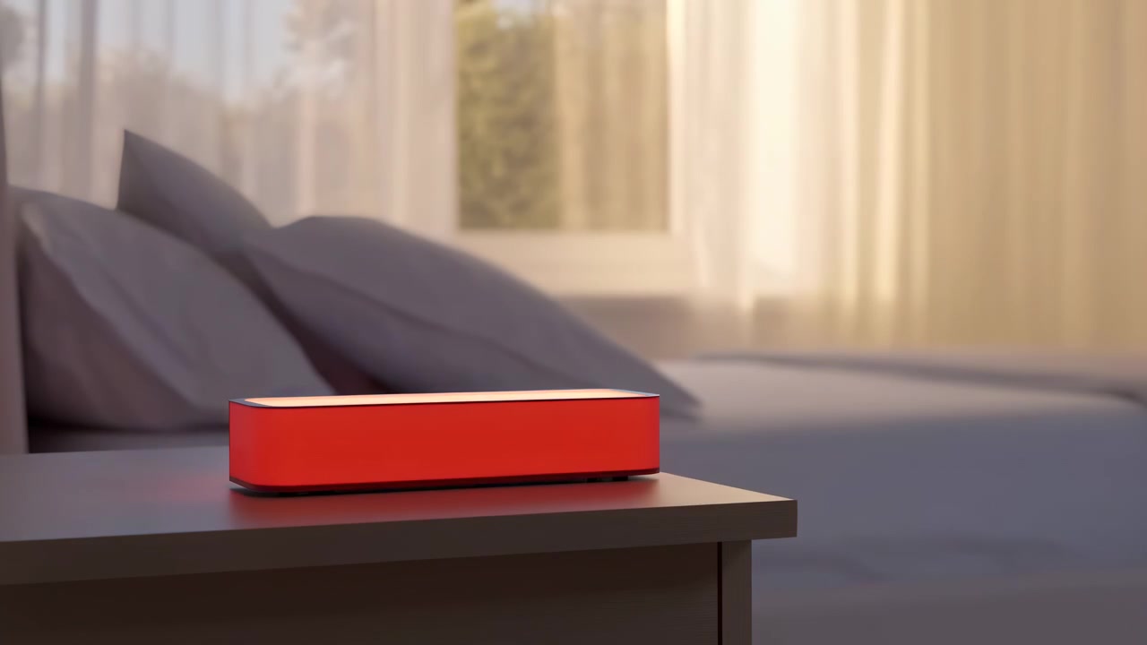 A quiet bedroom interior with a red rectangular object resting on a bedside table in the foreground, with a bed, pillows, and soft daylight through curtains